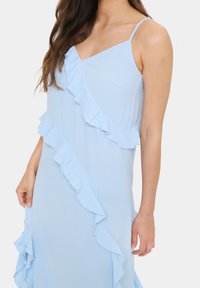 Rochie de un albastru deschis cu bretele subțiri, având accenturi cu volane pe față și pe lateral. Material moale și fluid cu o croială lejeră.
