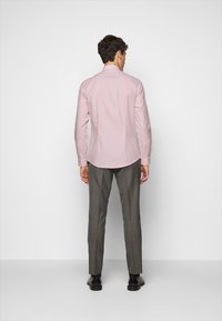 Camicia rosa chiaro con maniche lunghe, vestibilità slim, texture liscia, abbinata a pantaloni grigi a fantasia e scarpe nere.