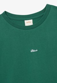T-shirt vert à col rond avec petit logo brodé "Blkvis" blanc sur la poitrine et étiquette beige à l'intérieur du col indiquant la marque et la taille L.