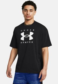 Melnas īsām piedurknēm T-kreklis ar lielu baltu Under Armour logotipu krūtīs. Audums izskatās gluds; brīva piegriezuma.