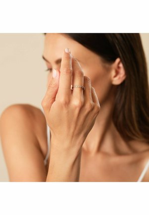 Goldring mit kleinen, klaren Edelsteinen, die entlang des Bandes angeordnet sind, getragen an einer Hand mit natürlichem Nagelfinish. Einfaches Design und elegante Details.