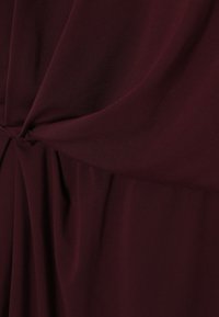 Bordeauxroter Stoff fällt weich und zeigt eine Drehung in der Mitte sowie eine glatte Textur mit dezentem Glanz und Falten.