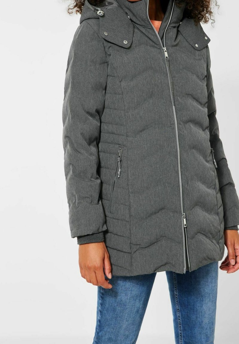 Grå vadderad jacka med dragkedja framtill, detaljstickning och huva med tryckknappar. Den har sidofickor med dragkedja och ribbade ärmslut.