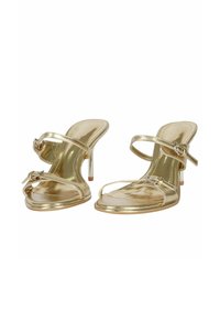 Sandali con tacco in metallo oro caratterizzati da un design open-toe, cinture alla caviglia regolabili e un elegante tacco a stiletto. Finitura liscia e lucida.