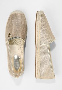 Zapatos tipo slip-on de lona en beige claro con detalles metálicos, parte superior texturizada, ribete de yute tejido y suela de goma. Con elástico en el empeine para mayor comodidad.
