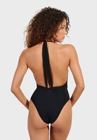 Crni jednodijelni kupaći kostim s dubokim dizajnom na leđima, tankim naramenicama i teksturiranim detaljima duž rubova. Glatka tkanina, visoko izrezane noge.