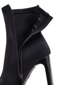 Botines de tacón alto negros con un upper de textil suave, que cuentan con una cremallera lateral y un tacón de charol brillante. Acentuados con detalles de costura.