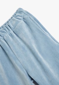Lyseblå fleecebukser med en blød tekstur, der har en elastisk talje og synlige sidesømme. Designet til komfort og varme.