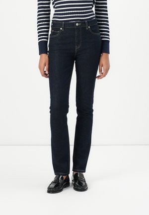 Person wearing dark blue straight-leg jeans, a navy and white striped long-sleeve top, and black shiny loafers on a white background.