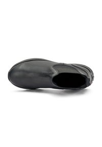 Zapato negro de cuero tipo slip-on con puntera redondeada, superficie texturada, paneles laterales elásticos y un detalle de logo en contraste en el talón.