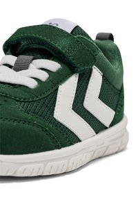 Grön sportskor med en kombination av mocka och meshmaterial, vita detaljer, ett kardborreband och en texturerad gummisula.