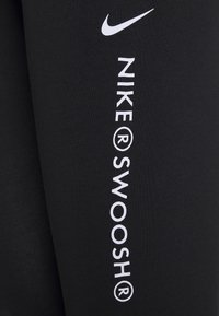 Svarta leggings av stretchigt material med vitt Nike-logga och texten "NIKE® SWOOSH®" tryckt vertikalt längs ena sidan.