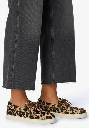 Feet wearing leopard-print lace-up casual shoes paired with cropped black denim jeans with raw hems.