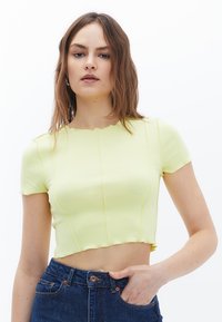 Gul cropped t-shirt lavet af blødt stof med korte ærmer, som har synlige sømlinjer og en bølget halsudskæring.
