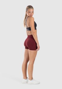 Zwarte sportbeha met dunne bandjes, gecombineerd met bordeauxrode high-waisted shorts. Witte sportschoenen met textuurdetail. Eenvoudig, aansluitend design.