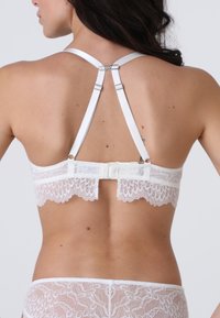 Bralette in pizzo bianco con spalline in satin regolabili. Presenta un bordo ondulato e una chiusura a gancio e occhiello sul retro per una vestibilità sicura.