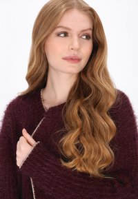 Burgundowa sweter dzianinowy o puszystej fakturze, z głębokim dekoltem w kształcie litery V i jasnym wykończeniem wzdłuż krawędzi.