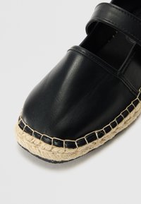 Zwarte leren espadrille met een ronde neus, voorzien van een natuurlijke jute zool en gestikte accenten. Twee banden boven de wreef.