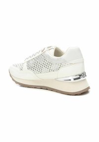 Zapato deportivo blanco con diseño perforado en los laterales, parte superior texturizada, acentos plateados y una suela beige gruesa con un detalle metálico en el talón.