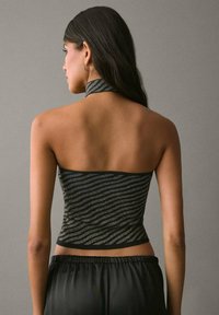 Čierny a zlatý prúžkovaný crop top s dizajnom na halter krk, ktorý má priliehavý tvar a hladkú textúru, kontrastujúci s jednofarebným pozadím.