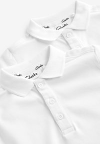 Deux chemises polo blanches en coton, avec des cols courts, des pattes de boutonnage à trois boutons et l'étiquette de la marque "Clarks" à l'intérieur du cou.