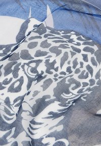Sciarpa con stampa leopardata caratterizzata da una texture liscia nei colori blu e bianco, che presenta un design prominente della faccia di un leopardo.
