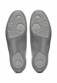 Szare podeszwy sportowych butów z okrągłymi i teksturowanymi wzorami; projekt bieżnika w zygzak i wyraźne cechy gumowego uchwytu dla lepszej przyczepności.