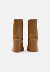 Brown suede ankle boots with a block heel, featuring a smooth texture and side zipper, designed for a fitted silhouette.