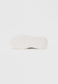 White sneaker sole with textured rubber, featuring a wavy pattern and embossed brand logo. Flat design, smooth finish, no visible laces.