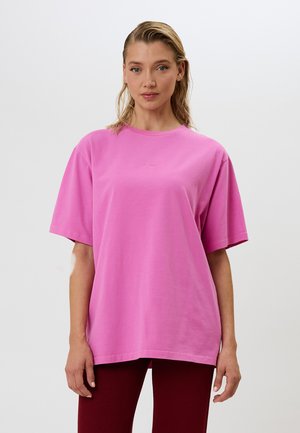 T-shirt oversize in cotone rosa con maniche corte, scollo rotondo e dettagli del logo discreti sul petto, abbinato a leggings borgogna a coste.