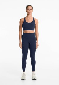 Soutien-gorge de sport navy et leggings taille haute en tissu extensible, avec une texture lisse et un design minimaliste, associés à des chaussures légères.