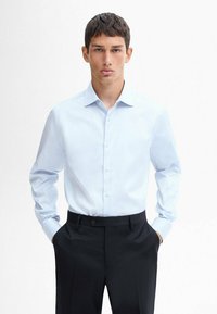 Light blue dress shirt with a button-down collar, long sleeves, and a smooth texture; paired with dark tailored pants.