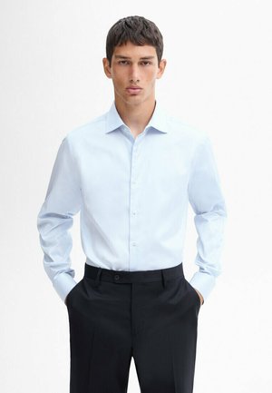 Lichtblauw overhemd met een button-down kraag, lange mouwen en een gladde textuur; gecombineerd met donkere, op maat gemaakte broek.