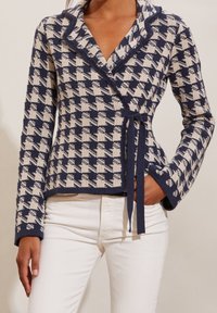 Marinblå och krämfärgad houndstooth-wraptröja med sjalkrage, knytstängning och långa ärmar, tillverkad av ett strukturerat stickat tyg.