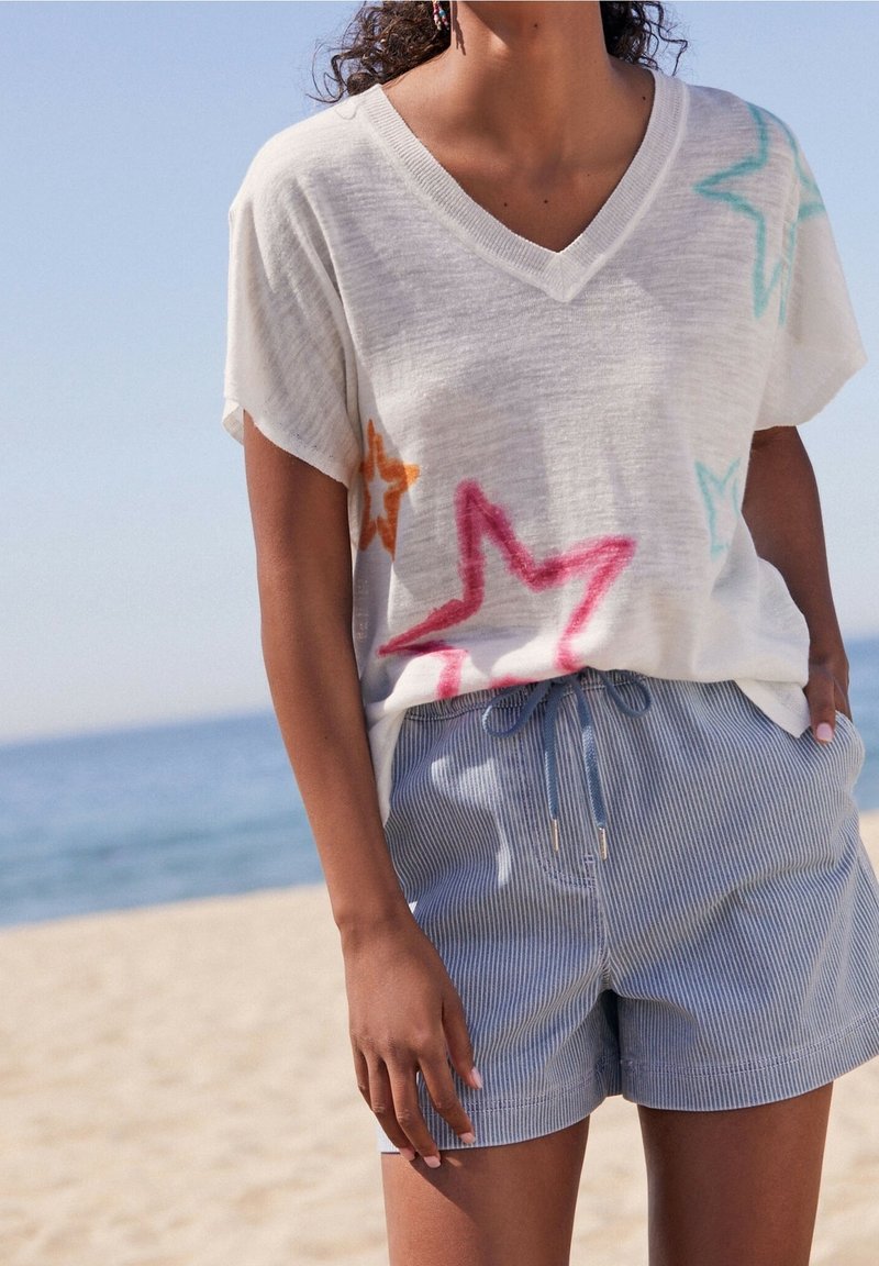 T-shirt blanc à manches courtes en V, orné de motifs d'étoiles colorées en rose, orange et bleu, associé à un short rayé bleu clair.