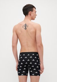 Fekete boxer alsónadrág fehér, ismétlődő háromszög mintával, testhezálló fazonban és rugalmas derékpánttal. A modell hátulról látható.