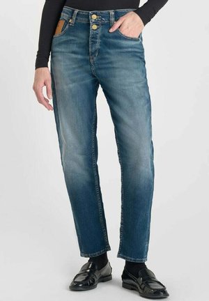 Jeans en denim bleu avec une coupe droite, présentant un délavage, deux poches avant, des boutons en métal et une étiquette en cuir marron à l'arrière.