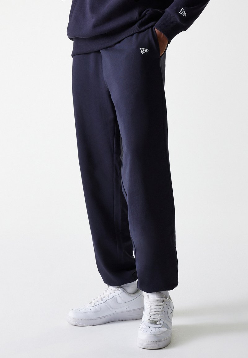 Navy sweatpants made of soft fabric, featuring side pockets and a small logo on the hip, paired with white high-top sneakers.