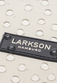 Beige szövet, textúrált felülettel, vízcseppekkel és fekete "LARKSON HAMBURG" logólappal, fehér felirattal és fényes részletekkel.