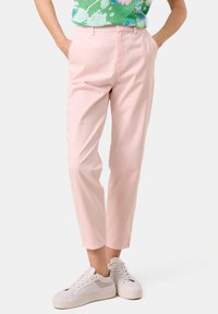 Hellrosa Freizeit-Hosen mit schmal zulaufendem Bein, aus Baumwolle, mit Seitentaschen und Gürtelschlaufen, kombiniert mit weißen Sneakers.