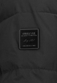 Black puffer jacket with a smooth texture. Features a square, embossed brand logo patch in black, prominently displayed on the fabric.