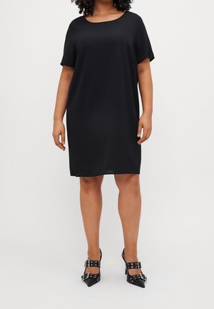 Zwart kort mouwen jurk met een losse pasvorm en een ronde halslijn. Glad, lichtgewicht materiaal. Gemaakt in combinatie met zwarte pumps met spitse neuzen en gespsdetails.