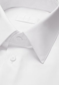 Knackiges weißes Hemd mit spitzem Kragen und zwei sichtbaren Knöpfen, ordentlich gefaltet und flach hingelegt.