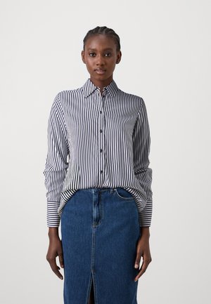 Button-up shirt featuring navy and white vertical stripes, a classic collar, button-front closure, and long sleeves; paired with a denim skirt.