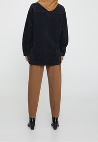 Chaqueta de corduroy azul marino oversize con capucha marrón, combinada con pantalones marrones ajustados y botas de tacón negras. Diseño texturizado y casual.