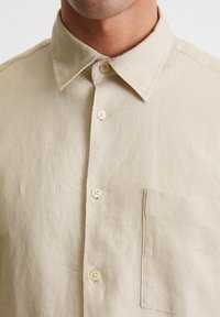 Beige linnen overhemd met een zachte textuur, button-down kraag en een enkele borstzak. Voorzien van lichtgekleurde knopen langs de knoopsluiting.