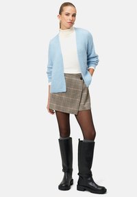 Jasnoniebieski dziany kardigan na białym golfie, połączony z brązową plisowaną spódnicą w kratę i czarnymi kozaki midi na masywnych podeszwach.