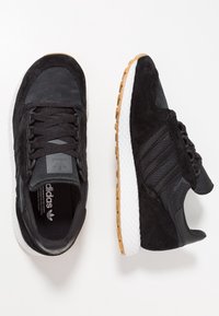 Musta mokka- ja verkkokankainen tennari, jossa on kolme mustaa raitaa, valkoinen kumipohja ja kumipohjallinen. Parannettu pito ja pehmustettu sisäosa.