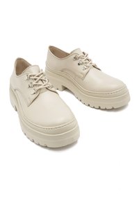 Beżowe skórzane buty o gładkim wykończeniu, okrągłym nosku, sznurowanym fasonie oraz grubej gumowej podeszwie z rowkami zapewniającymi przyczepność.