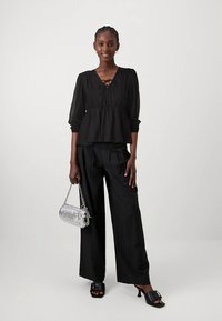 Svart peplumbluse med knytedetalj; svarte vidbukse; sølvfarget håndveske med kjedestropp; svarte sandaler med blokkhæl.